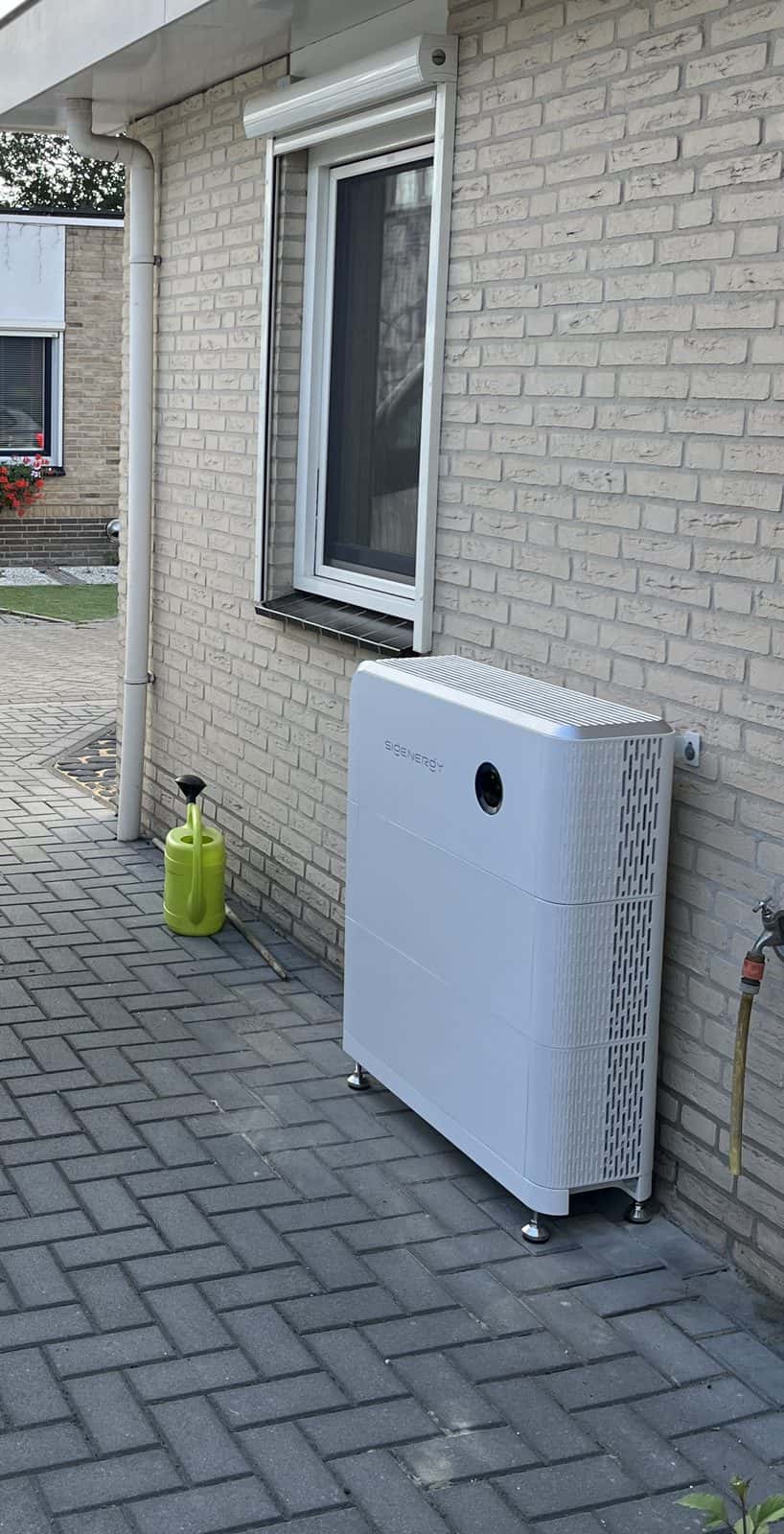Sigenergy thuisbatterij buiten tegen een lichte bakstenen gevel naast de oprit