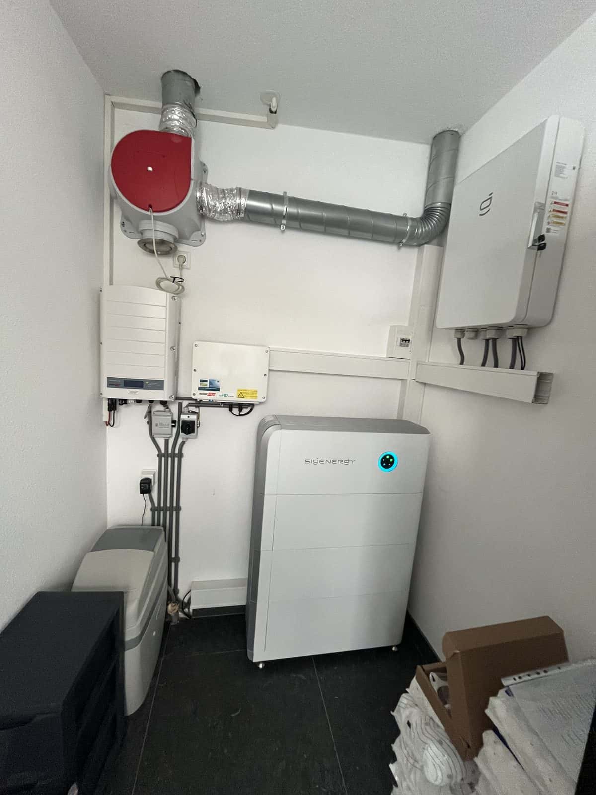 Complete Sigenergy-installatie in een witte technische ruimte: controller aan de wand en batterij op de vloer